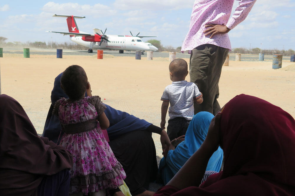 [航空機を遠くから眺める、子どもを含む難民の写真]